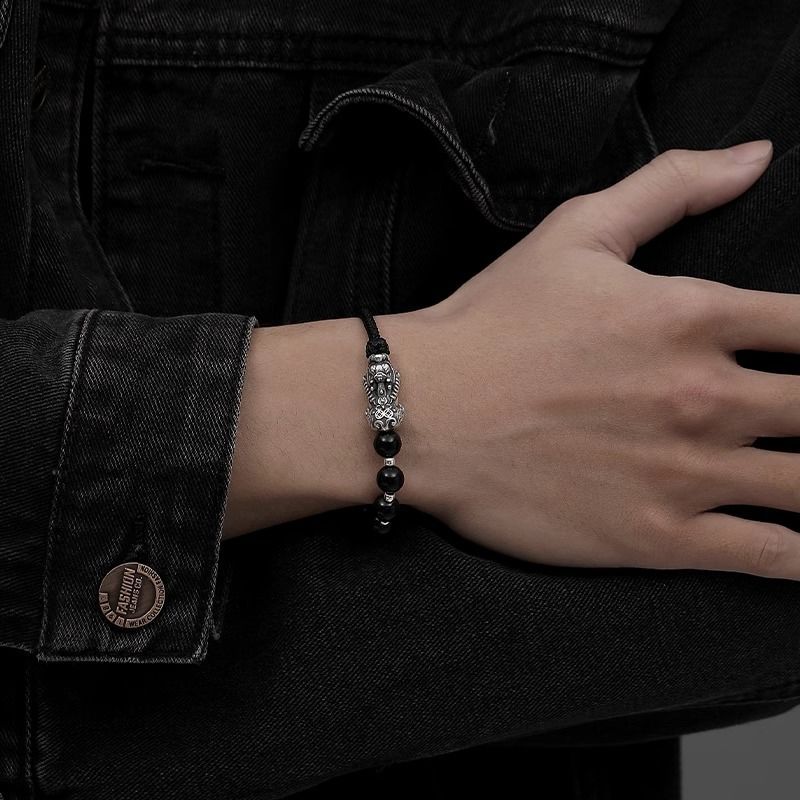 Bracelet tibétain Pi Xiu en pierres noires et fil rouge sur poignet, style unisexe, détails argentés.