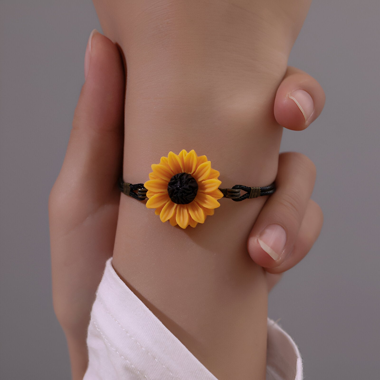 Bracelet noir fin en microfibre avec charm tournesol jaune vif porté au poignet.