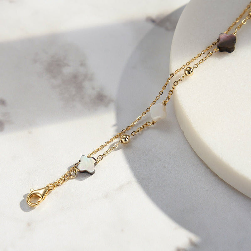 Bracelet double chaîne dorée avec deux trèfles en nacre blanche et noire, style délicat et raffiné.