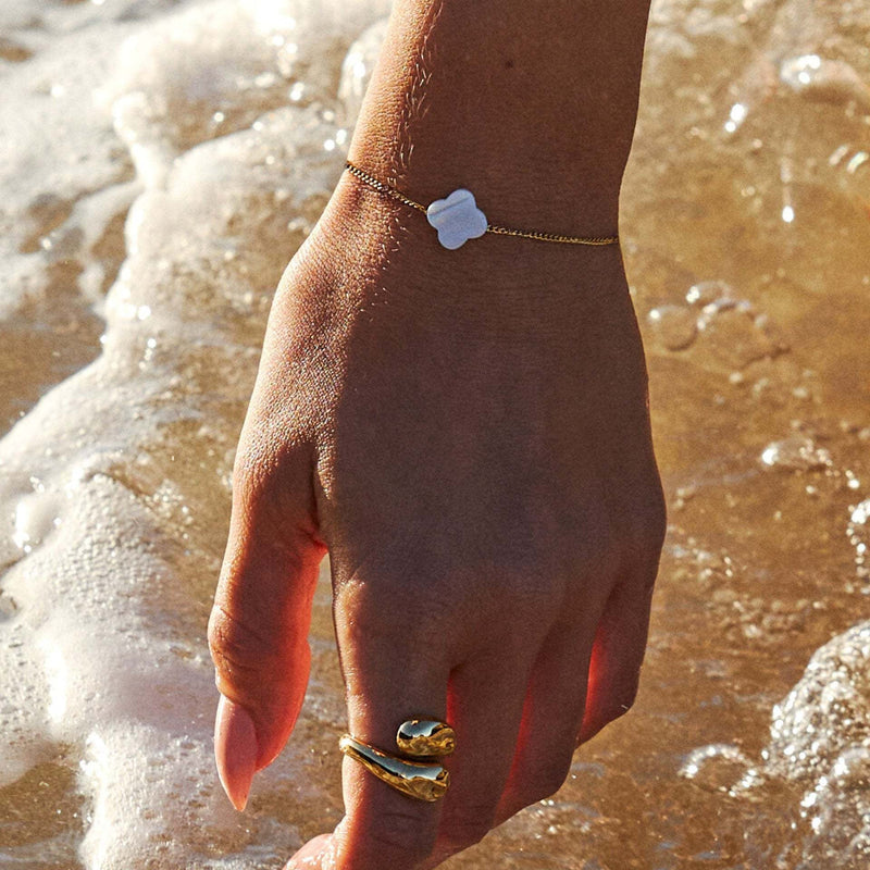 Bracelet fin chaîne dorée avec pendentif trèfle en pierre blanche naturelle, ajustable, porté au poignet féminin au bord de.