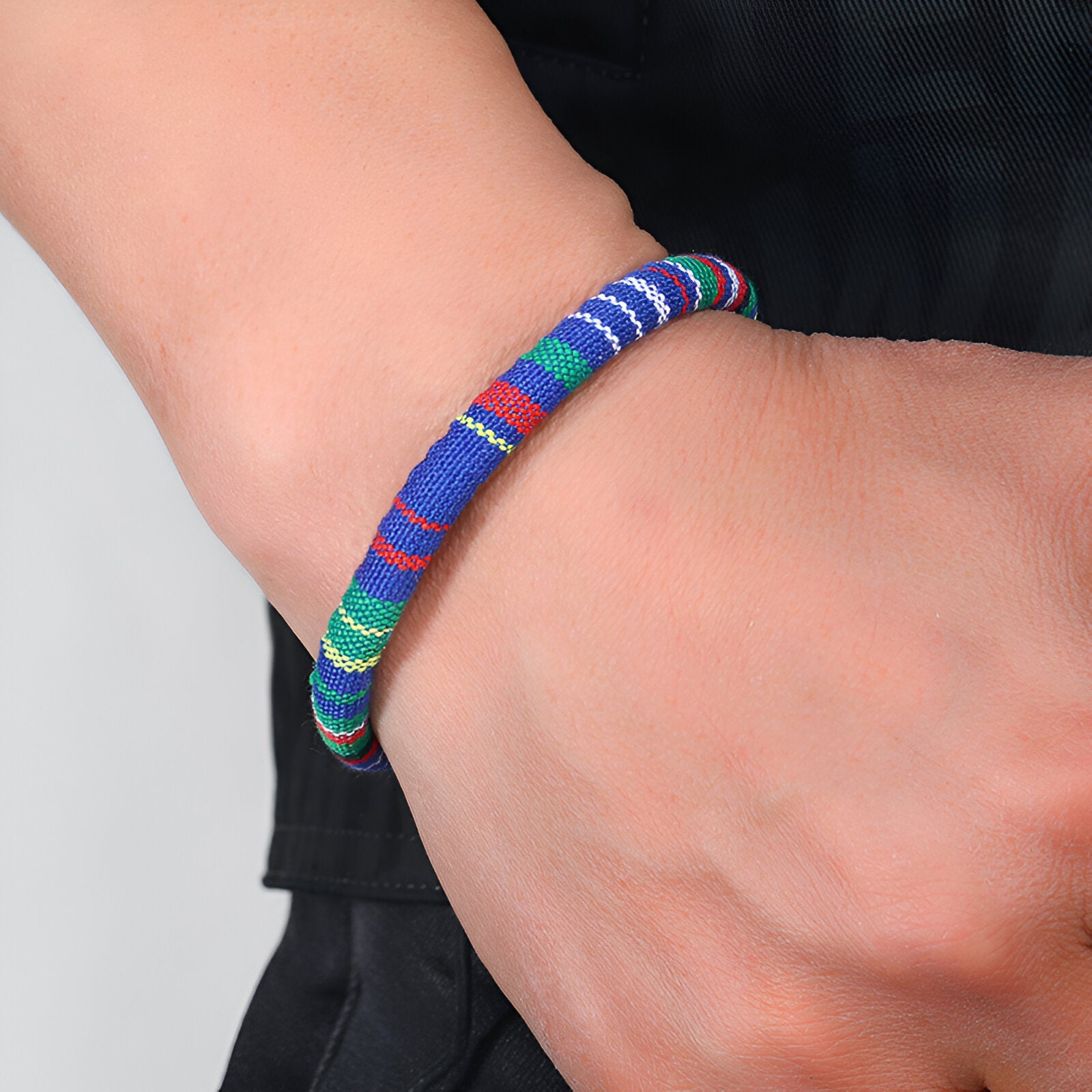 Bracelet tressé en coton aux motifs colorés bleus, verts et rouges porté au poignet.