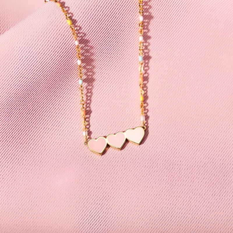 Bracelet en or avec trois cœurs alignés sur chaîne fine délicate posée sur tissu rose.