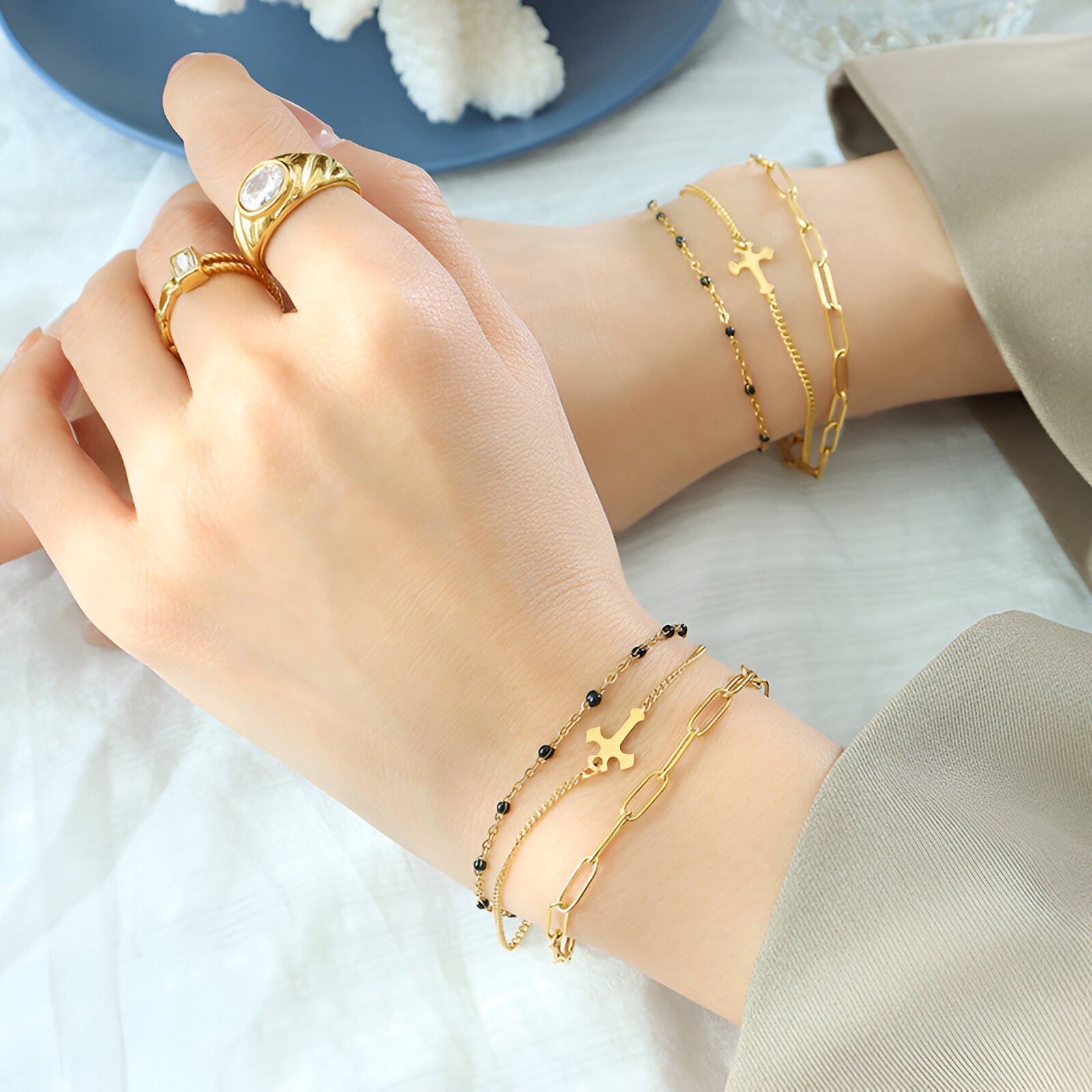 Bracelet triple mailles en titane plaqué or avec motif croix délicat sur poignet féminin.
