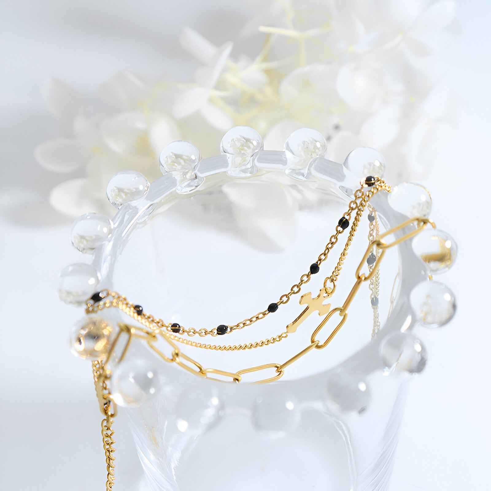 Bracelet triple mailles doré à motif croix en titane plaqué or sur support transparent.