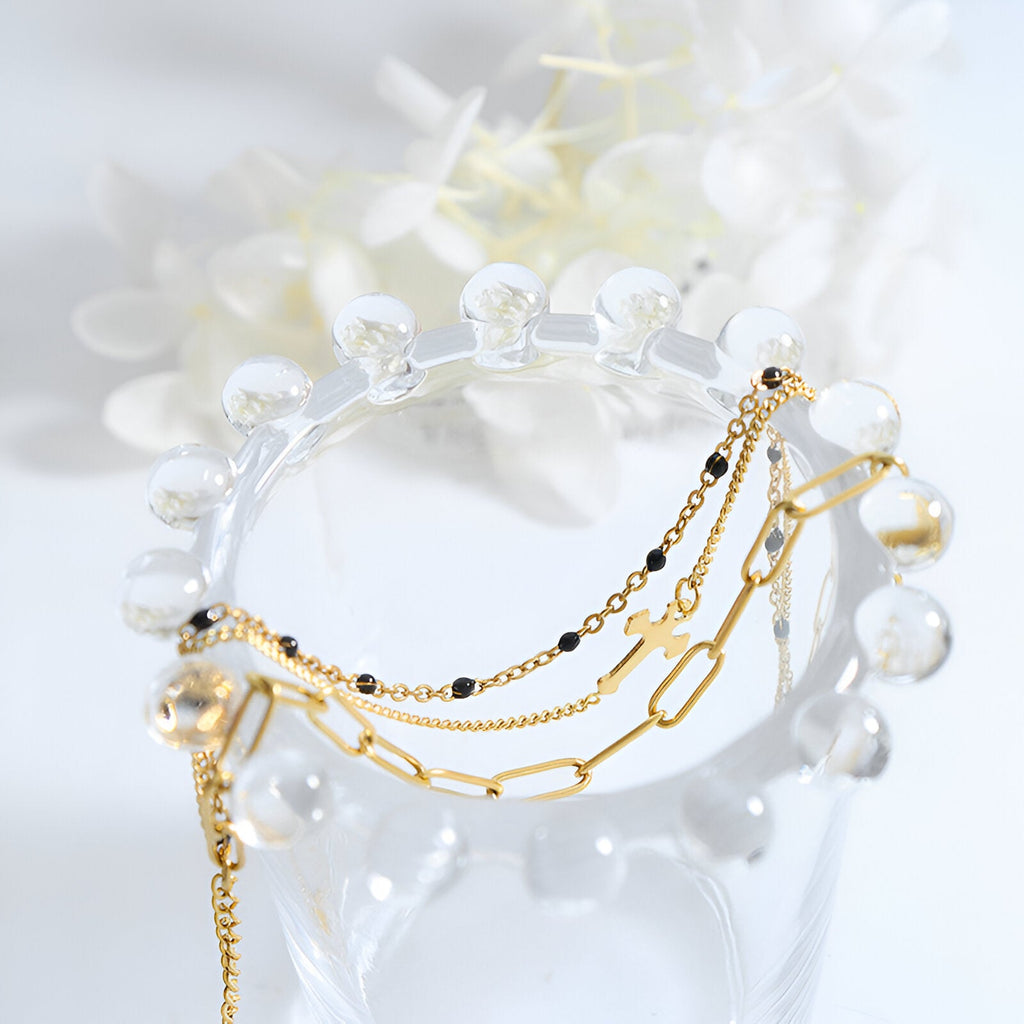 Bracelet triple mailles doré à motif croix en titane plaqué or sur support transparent.