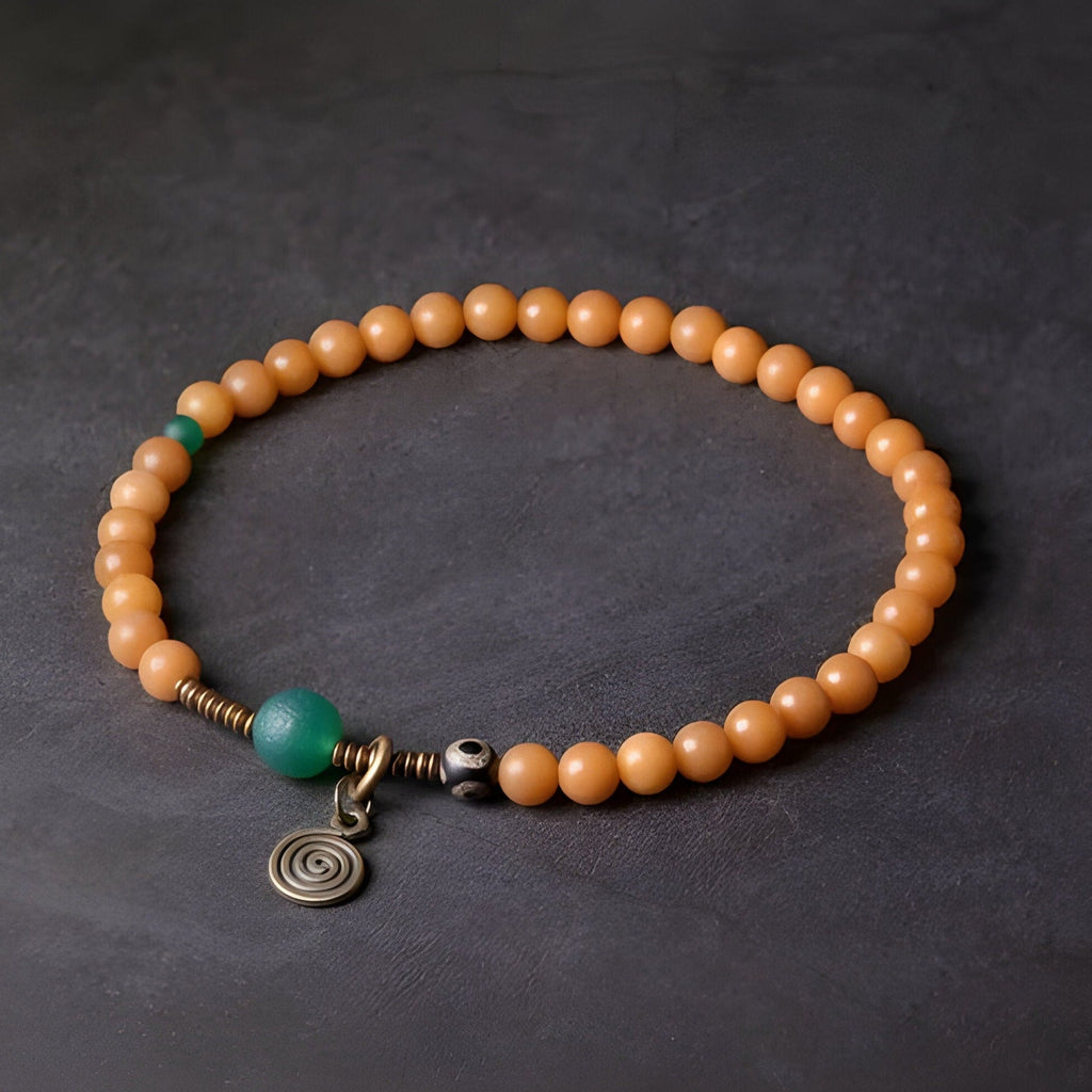 Bracelet femme en graines de Bodhi orange avec perles d'agate vertes et pendentif spirale en métal antique.