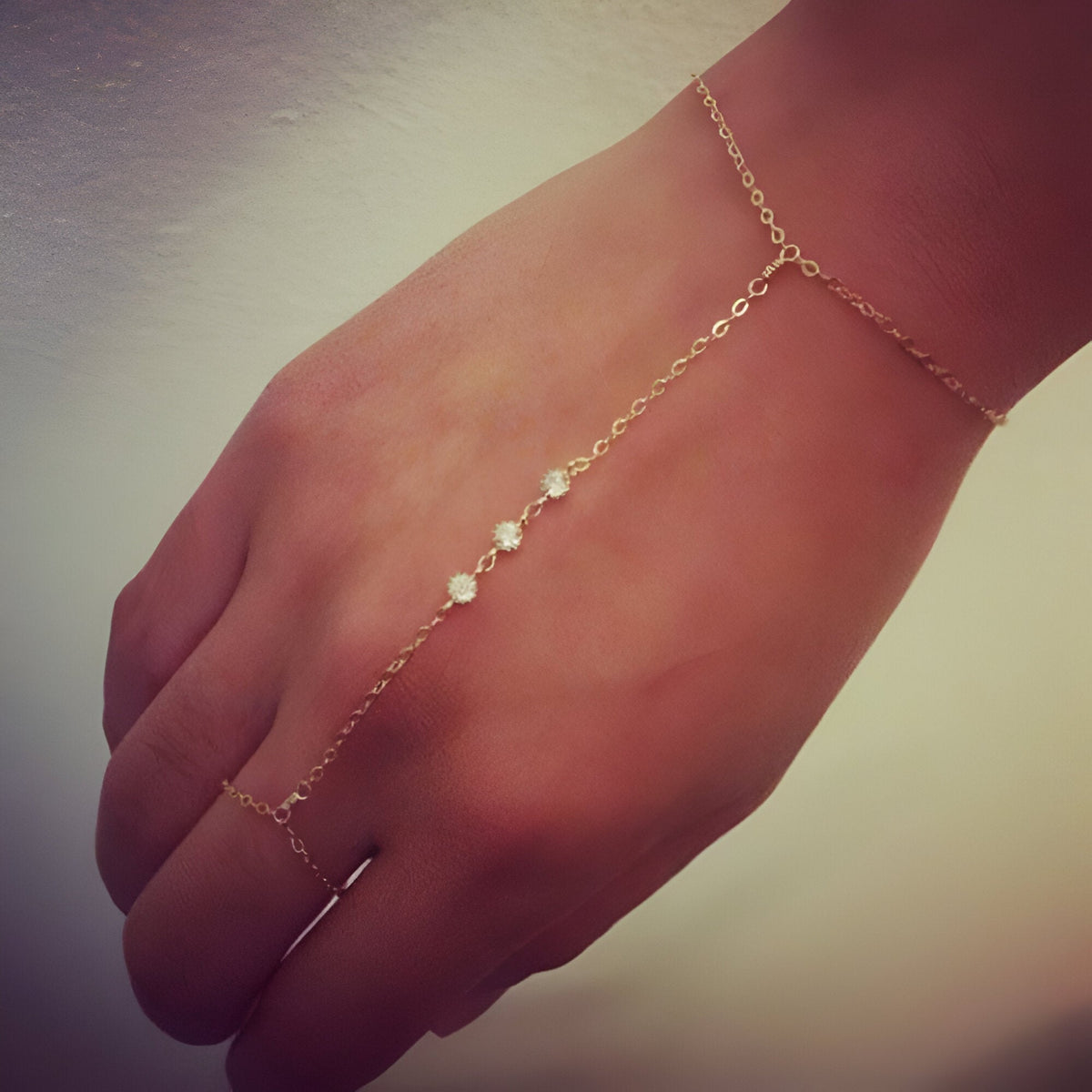 Bijou de main or fin avec zirconiums, chaîne fine reliant doigt et poignet, style délicat et élégant.