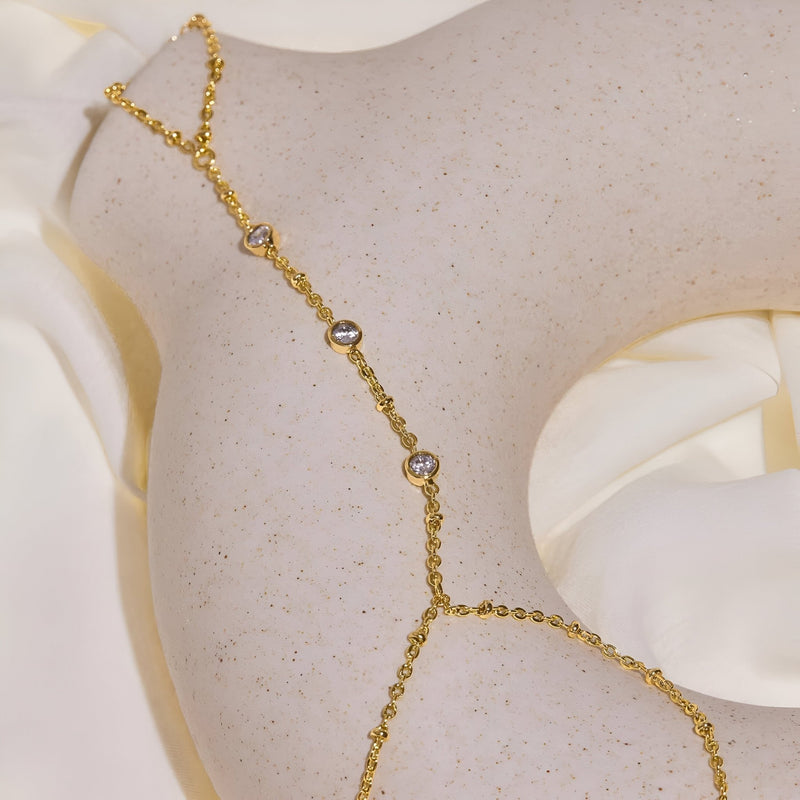 Bijou de main en acier inoxydable doré avec zirconiums, chaîne fine reliant doigt et poignet.