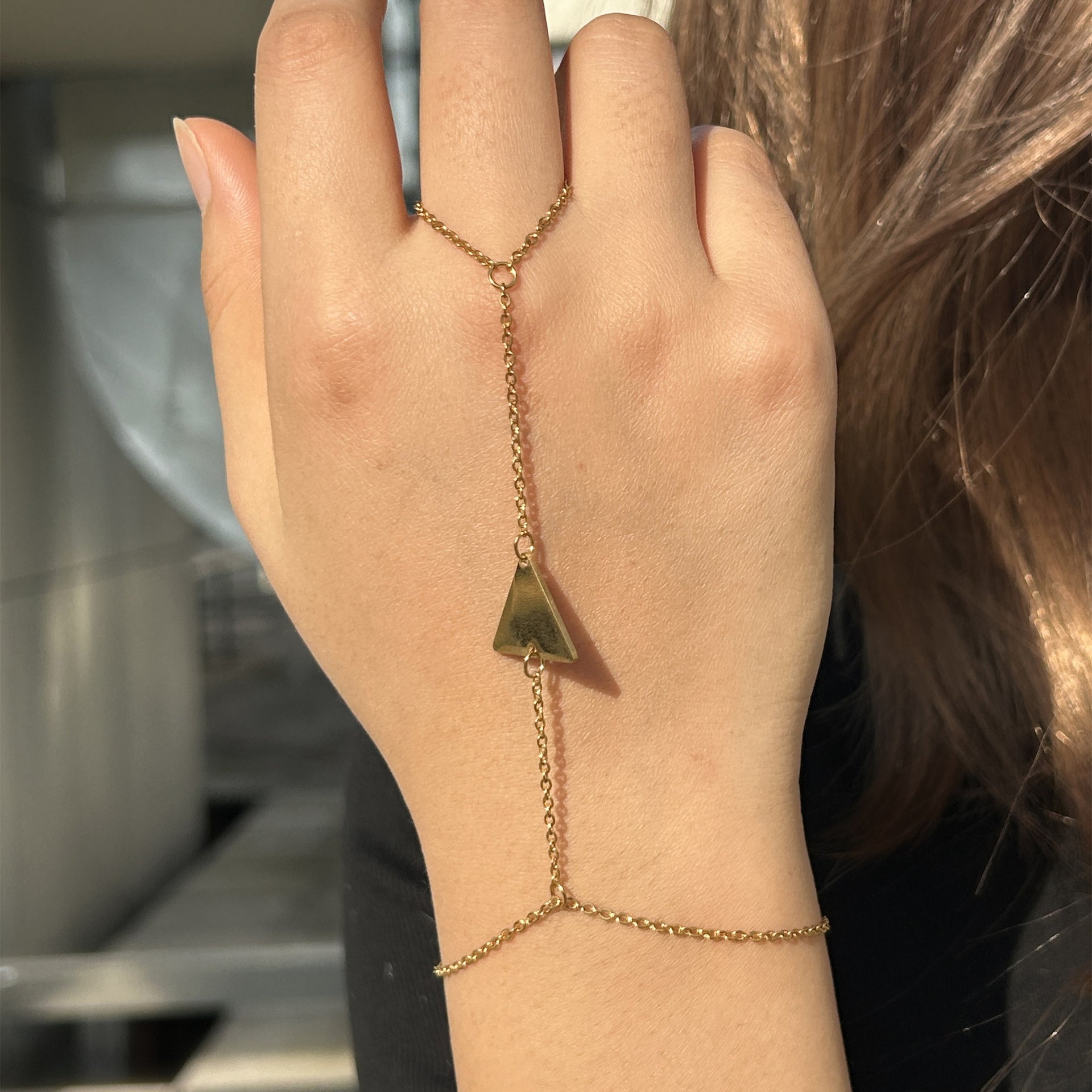 Bijou de main en acier inoxydable doré avec motif triangle et chaîne fine élégante.