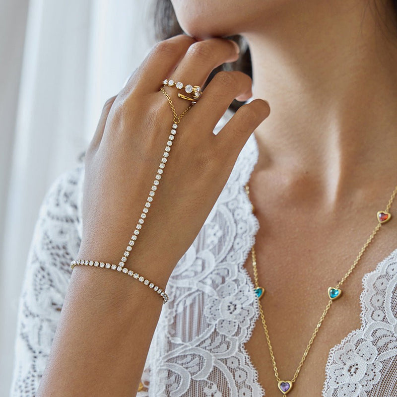 Chaîne de main dorée à l’or fin ornée de petits zircons scintillants, design élégant reliant bague et bracelet, porté sur.