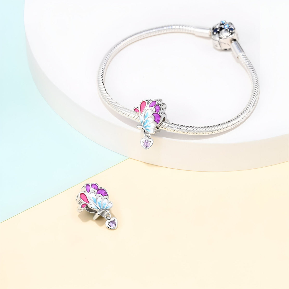 Charm pendentif aile de papillon argenté avec détails roses et bleus, sur bracelet serpent argenté.