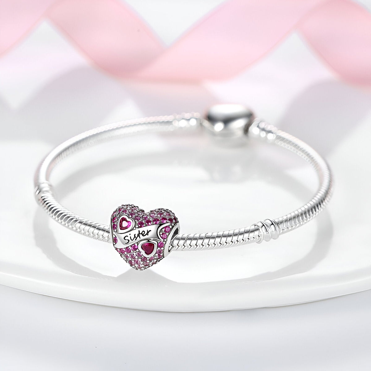 Bracelet argenté avec charm cœur rose et inscription "Sœur" en lettres rouges.