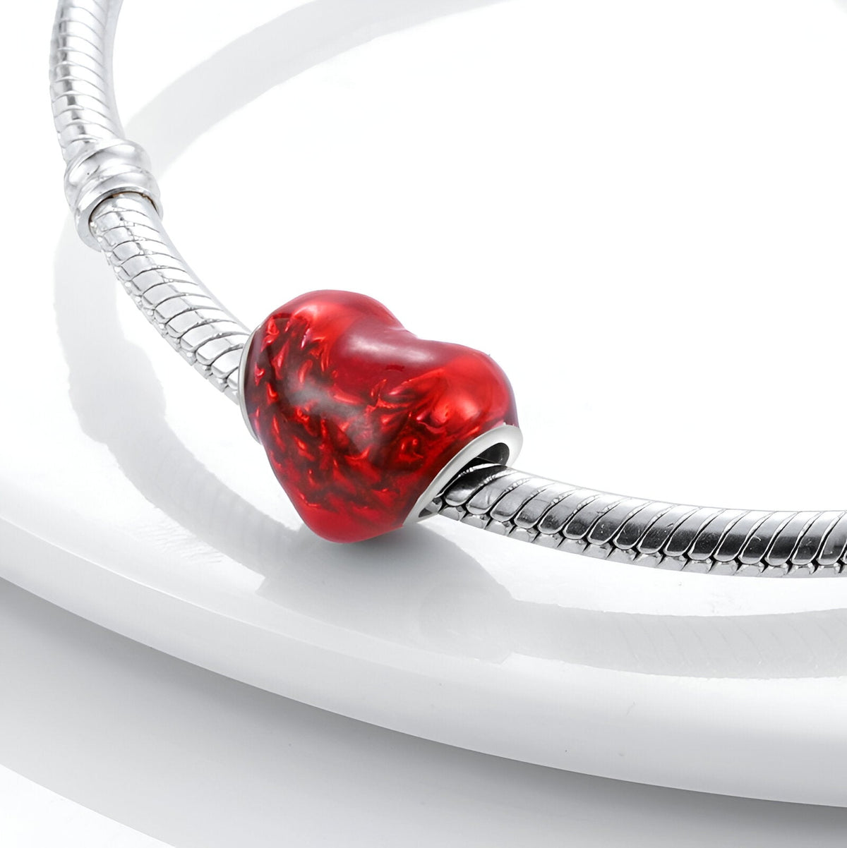 Charm en forme de cœur rouge vif avec texture marbrée sur bracelet serpent argenté.