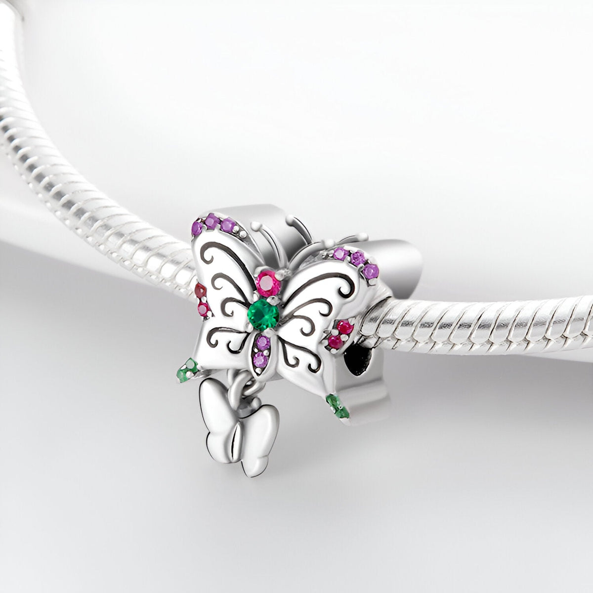 Charm argenté duo papillons avec strass verts et violets, détail ailes stylisées.