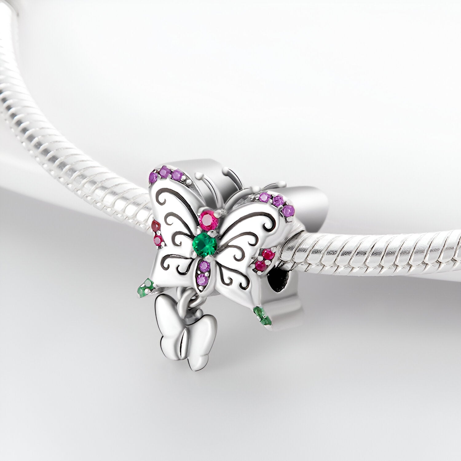 Charm argenté duo papillons avec strass verts et violets, détail ailes stylisées.