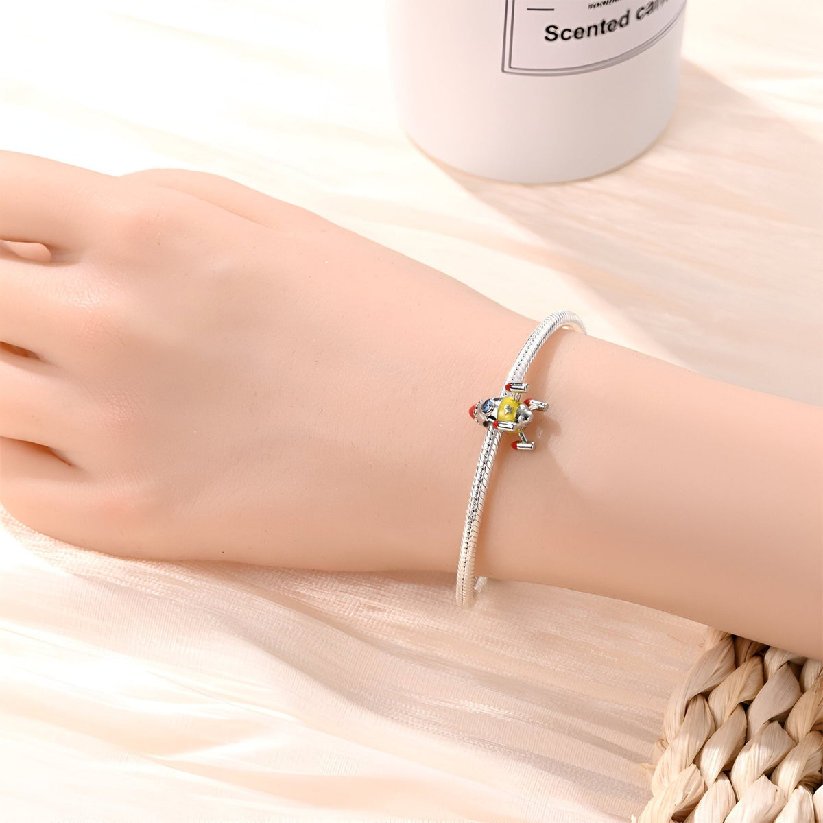 Bracelet en métal argenté avec charm fusée spatiale colorée et détails fins.