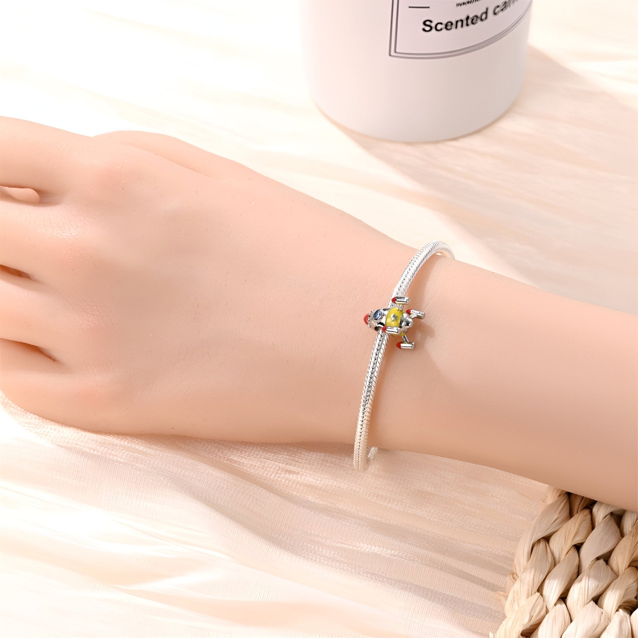 Bracelet en métal argenté avec charm fusée spatiale colorée et détails fins.