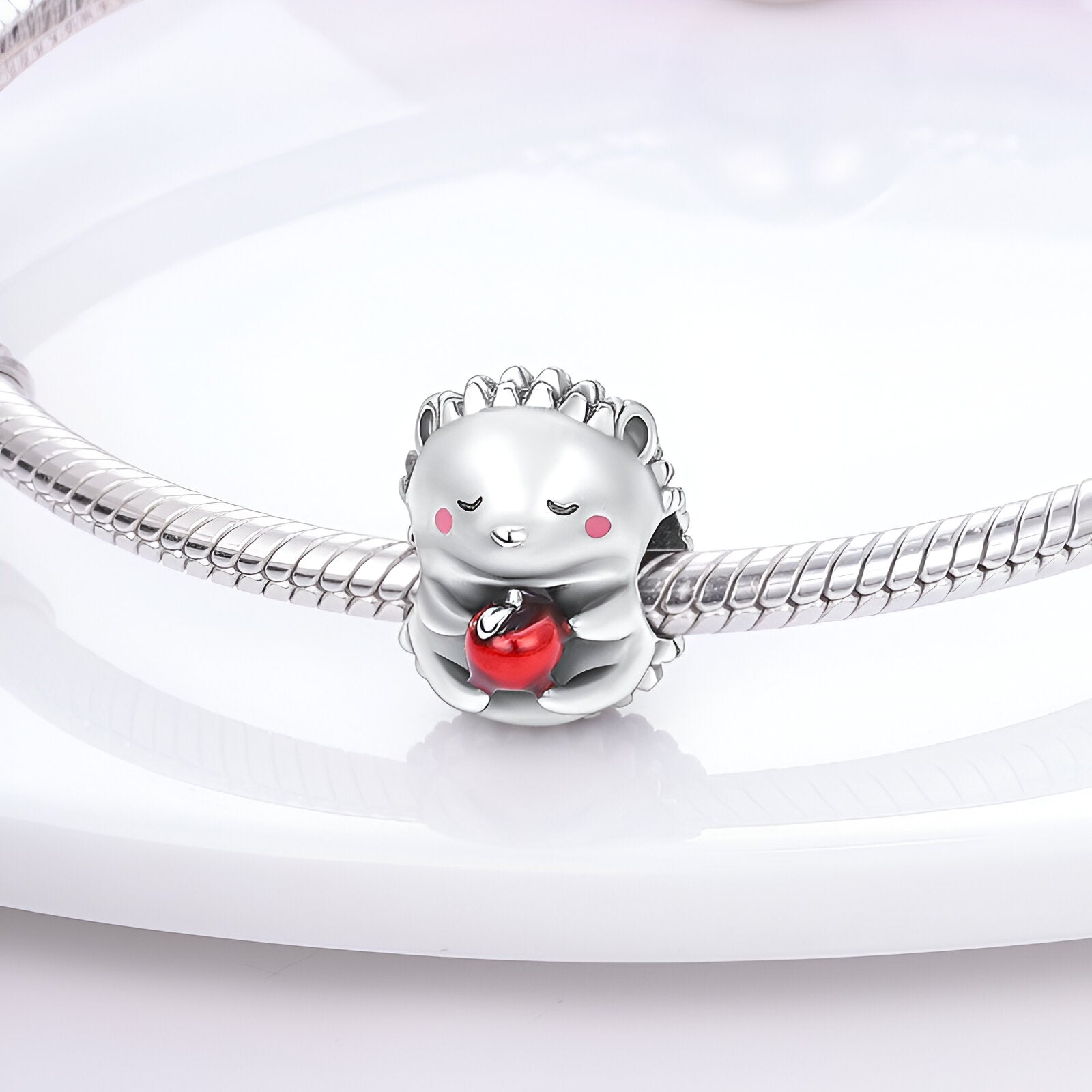 Charm en forme de hérisson argenté tenant une pomme rouge sur un bracelet serpent en argent.