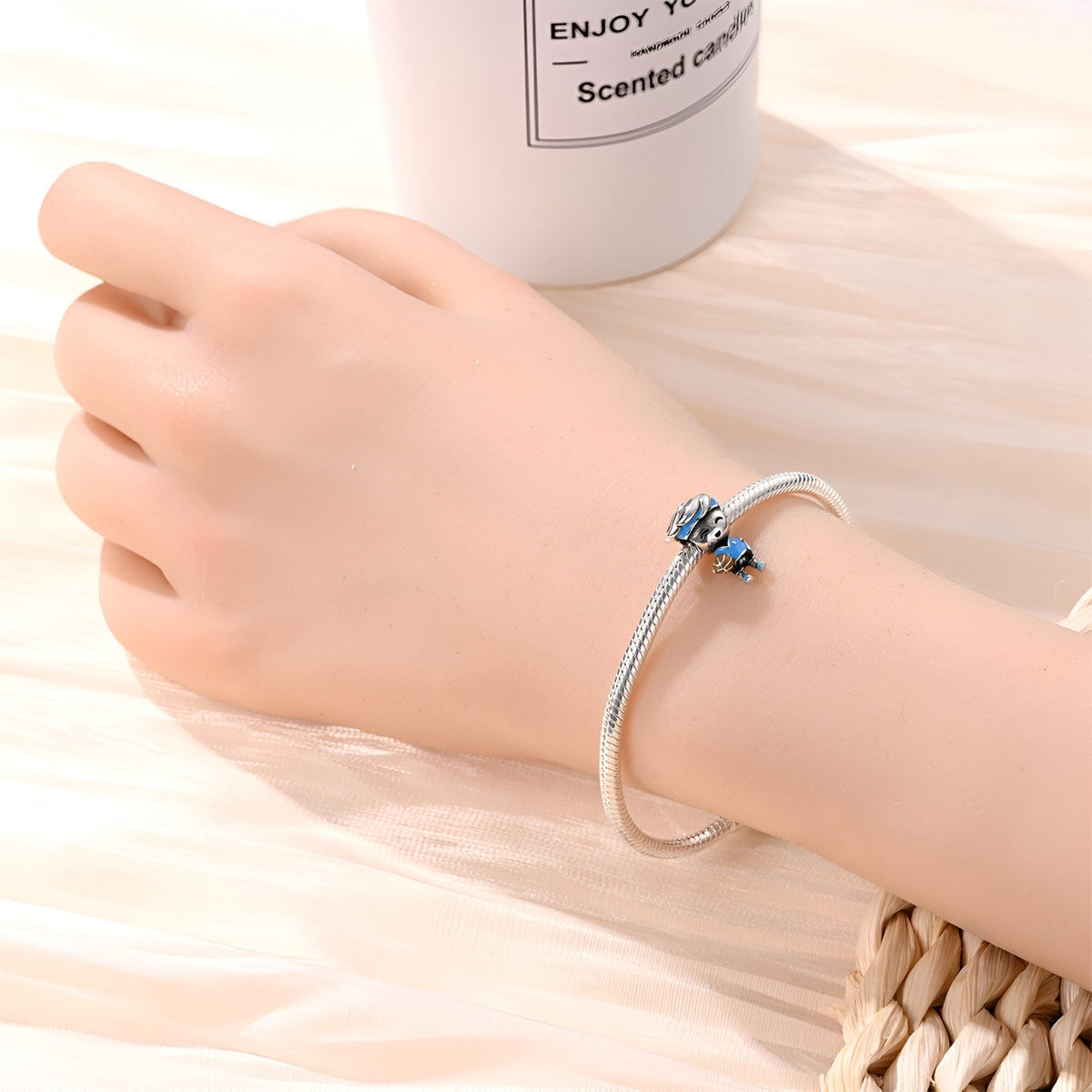 Bracelet argenté rigide avec charm joueur de basket bleu sur main féminine, fond clair en bois.