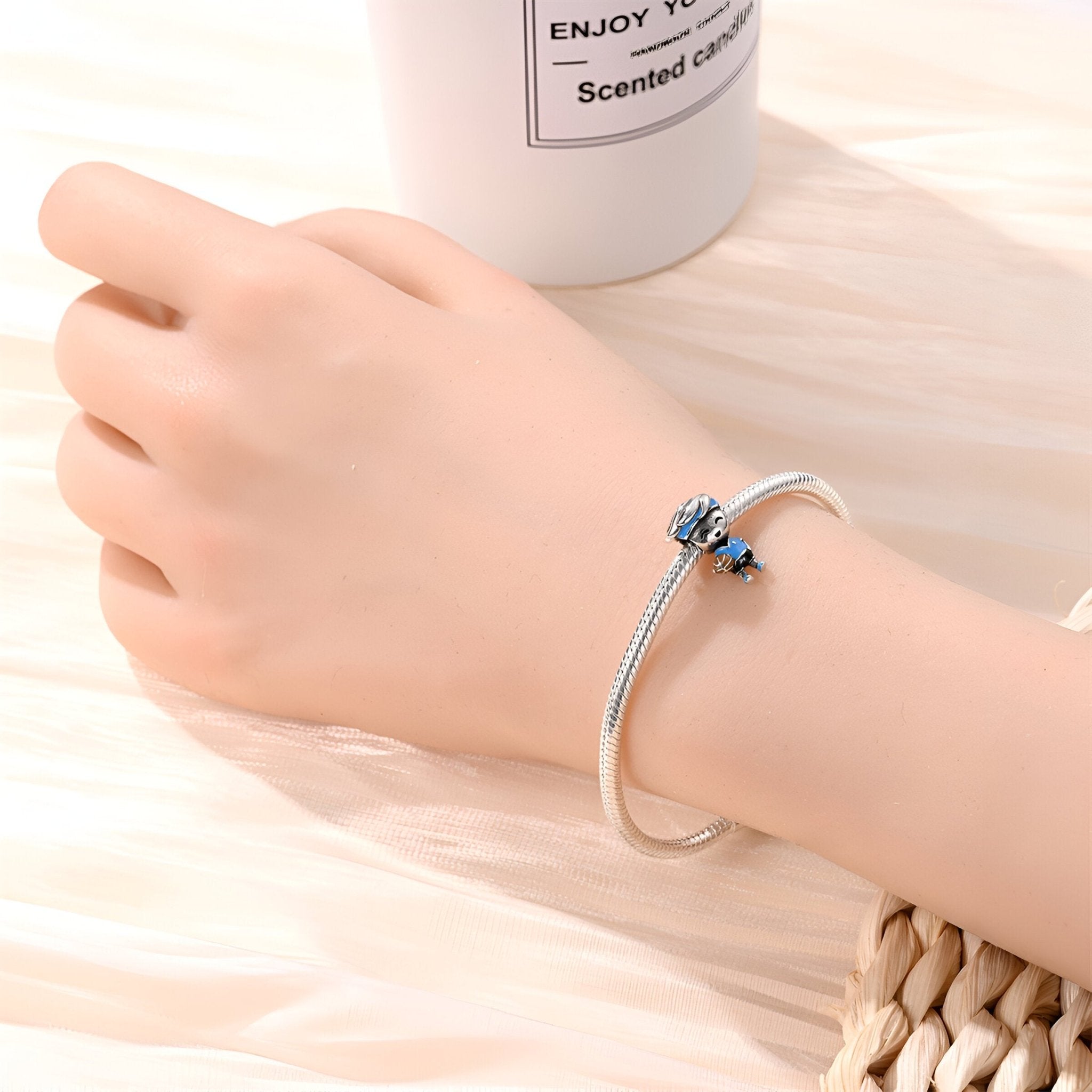 Bracelet argenté rigide avec charm joueur de basket bleu sur main féminine, fond clair en bois.