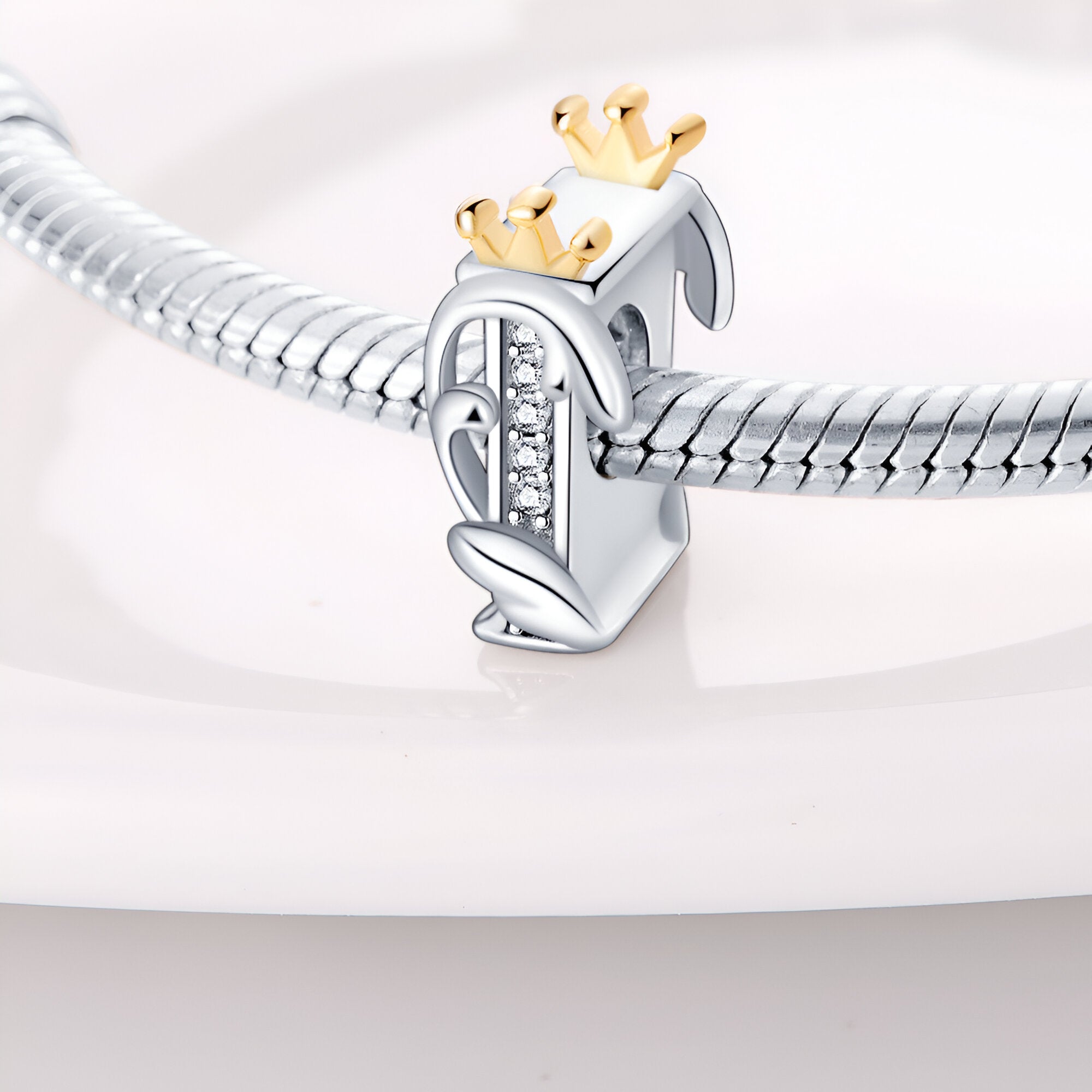 Charm lettre I en argent orné de petites pierres blanches avec couronne dorée sur un bracelet serpent argenté.