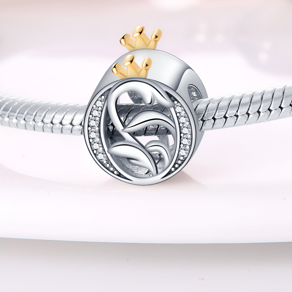 Charm lettre O argenté avec couronne dorée et détails feuille, serti de petits cristaux blancs.