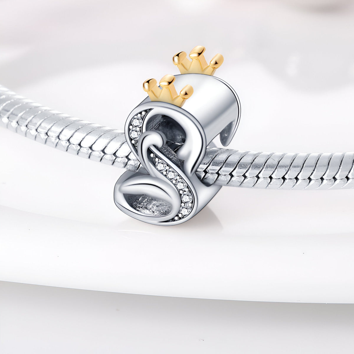 Charm lettre S en argent avec couronne dorée et détails en cristaux sur bracelet serpent en argent.