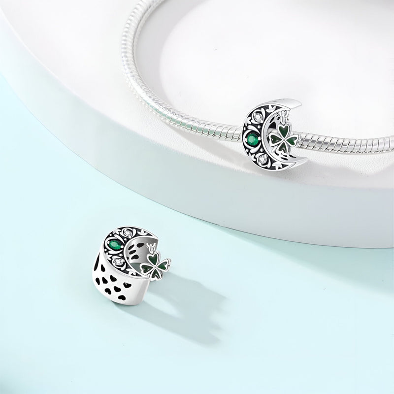 Charm argenté en forme de lune ajourée avec trèfle et pierre verte sur bracelet argenté.