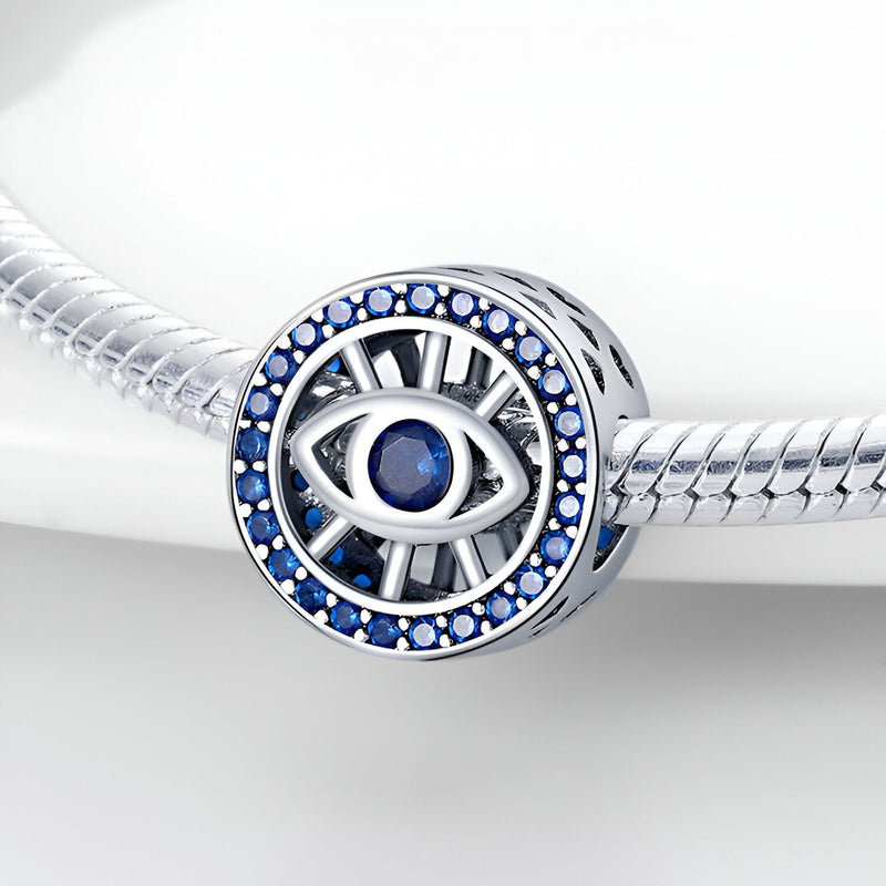 Charm rond en argent avec un œil bleu central et strass bleus autour, style protecteur.