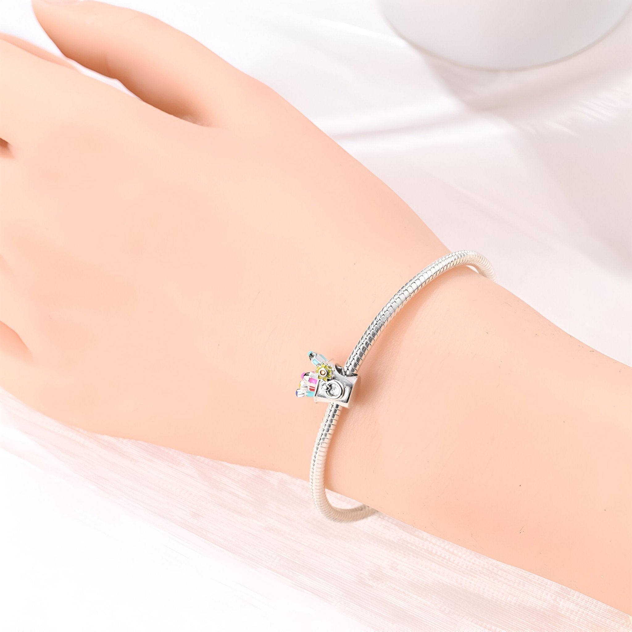Bracelet argenté fin avec charme miniature en forme d'outils de peinture colorés.