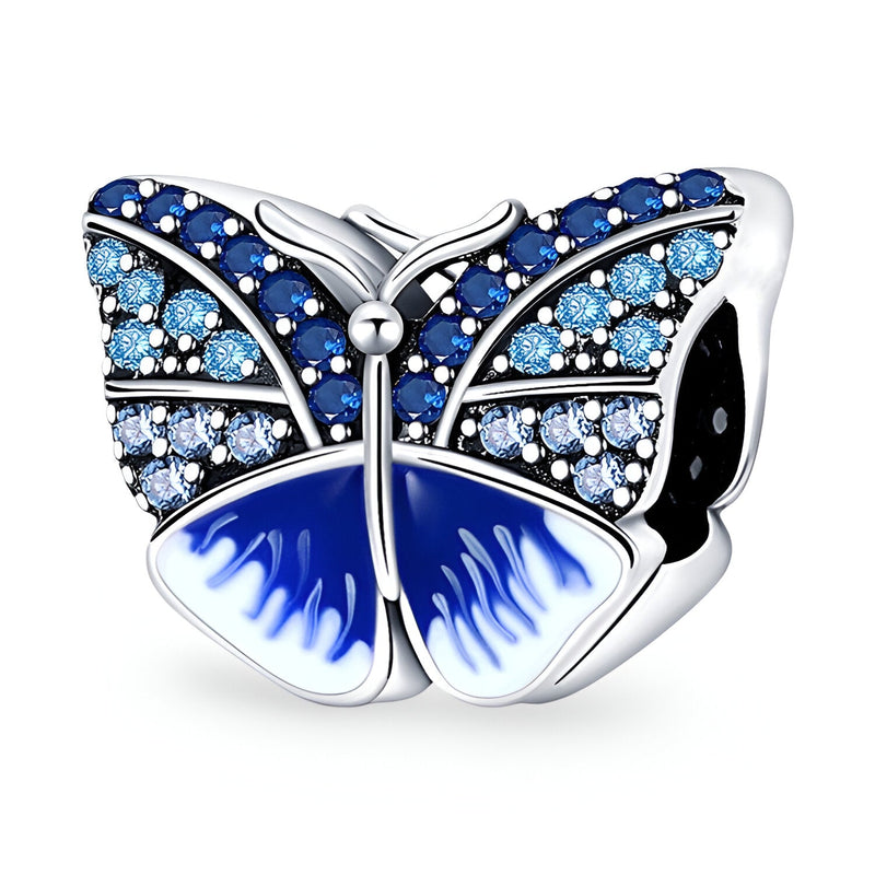 Charm papillon en métal argenté avec strass bleus et émail bleu dégradé sur les ailes.