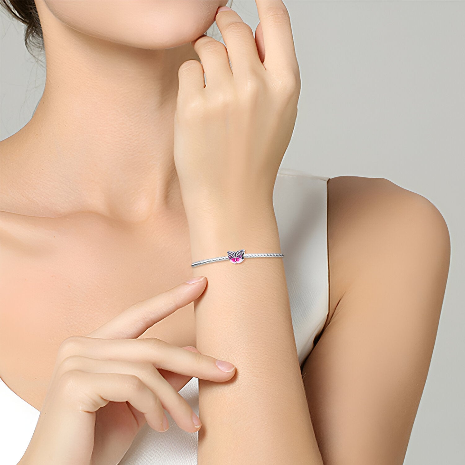 Bracelet fin argenté avec charm papillon rose délicat sur poignet féminin.
