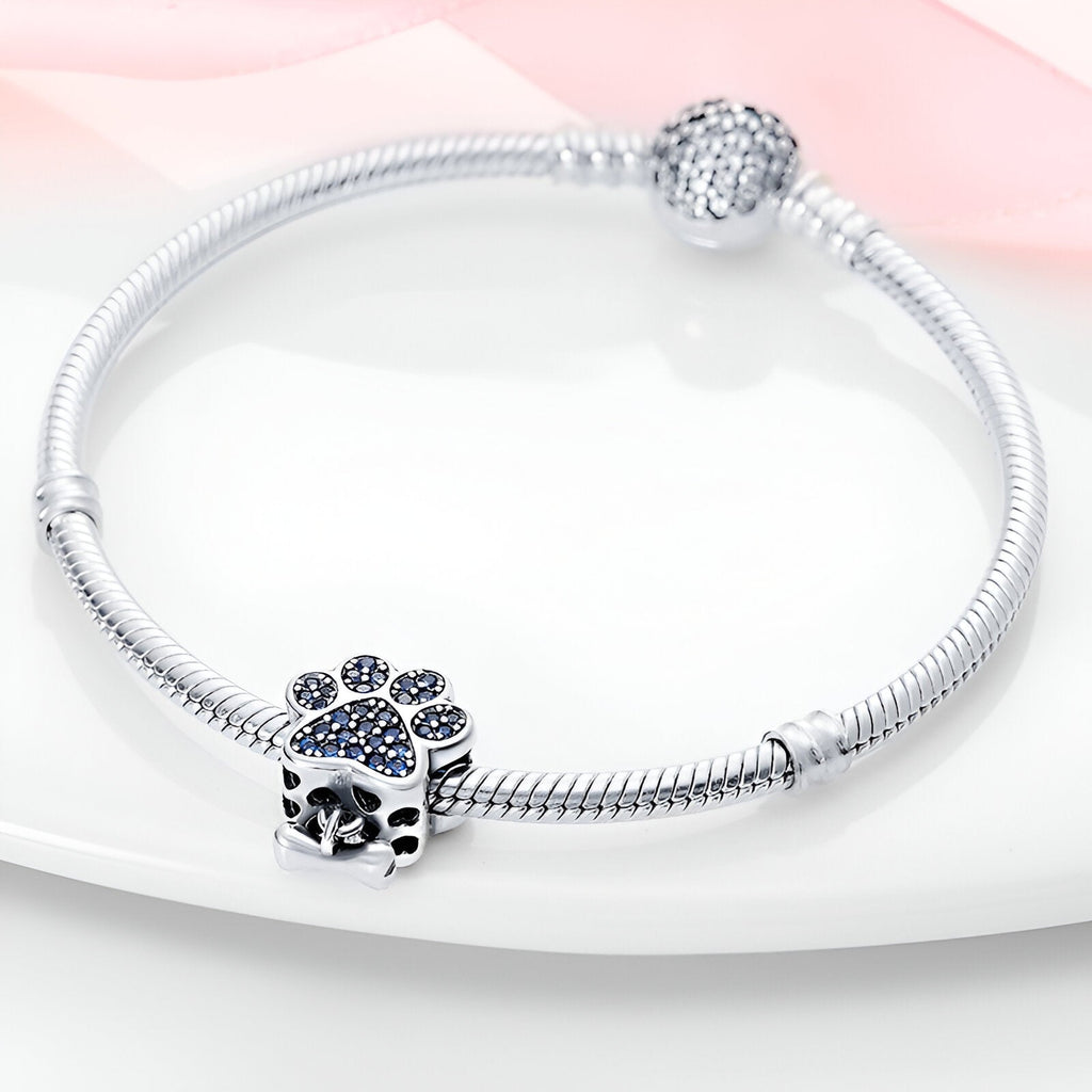 Bracelet argent avec charm en forme de patte de chien et os serti de pierres bleues.