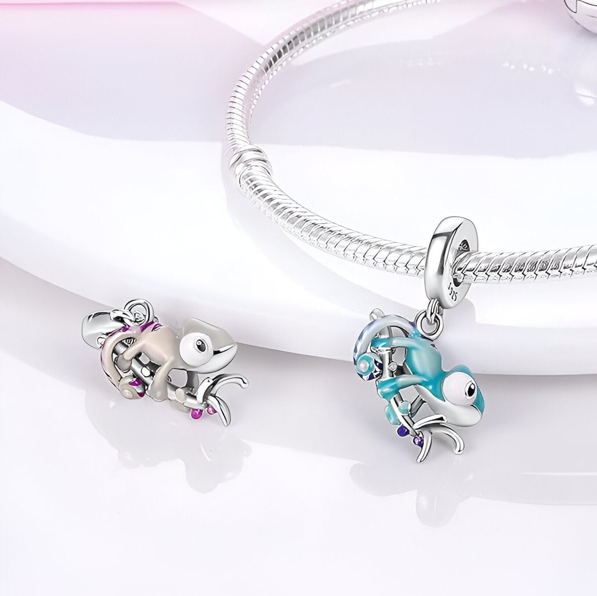 Charm caméléon argent avec détails rose et turquoise, pendentif suspendu à un bracelet serpent argenté.