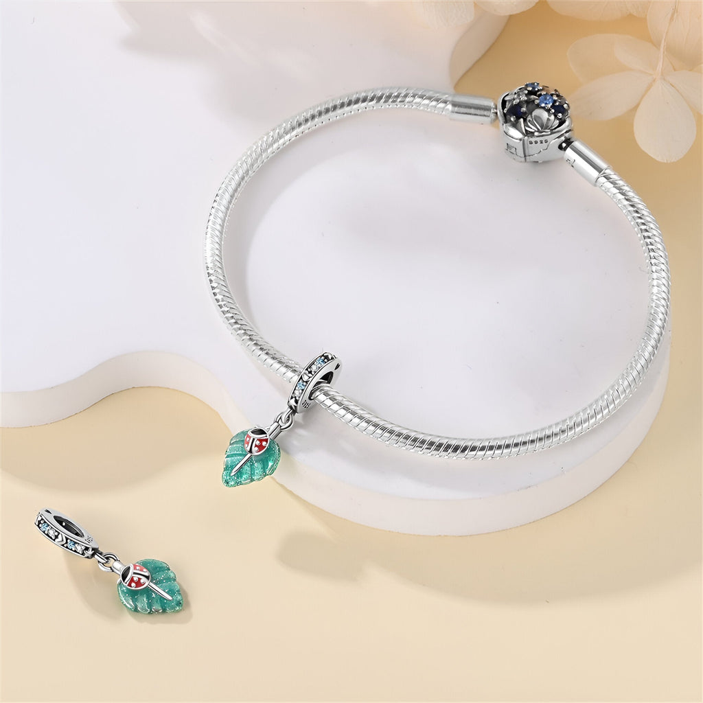 Bracelet argenté avec charm coccinelle rouge sur feuille verte éclatante.