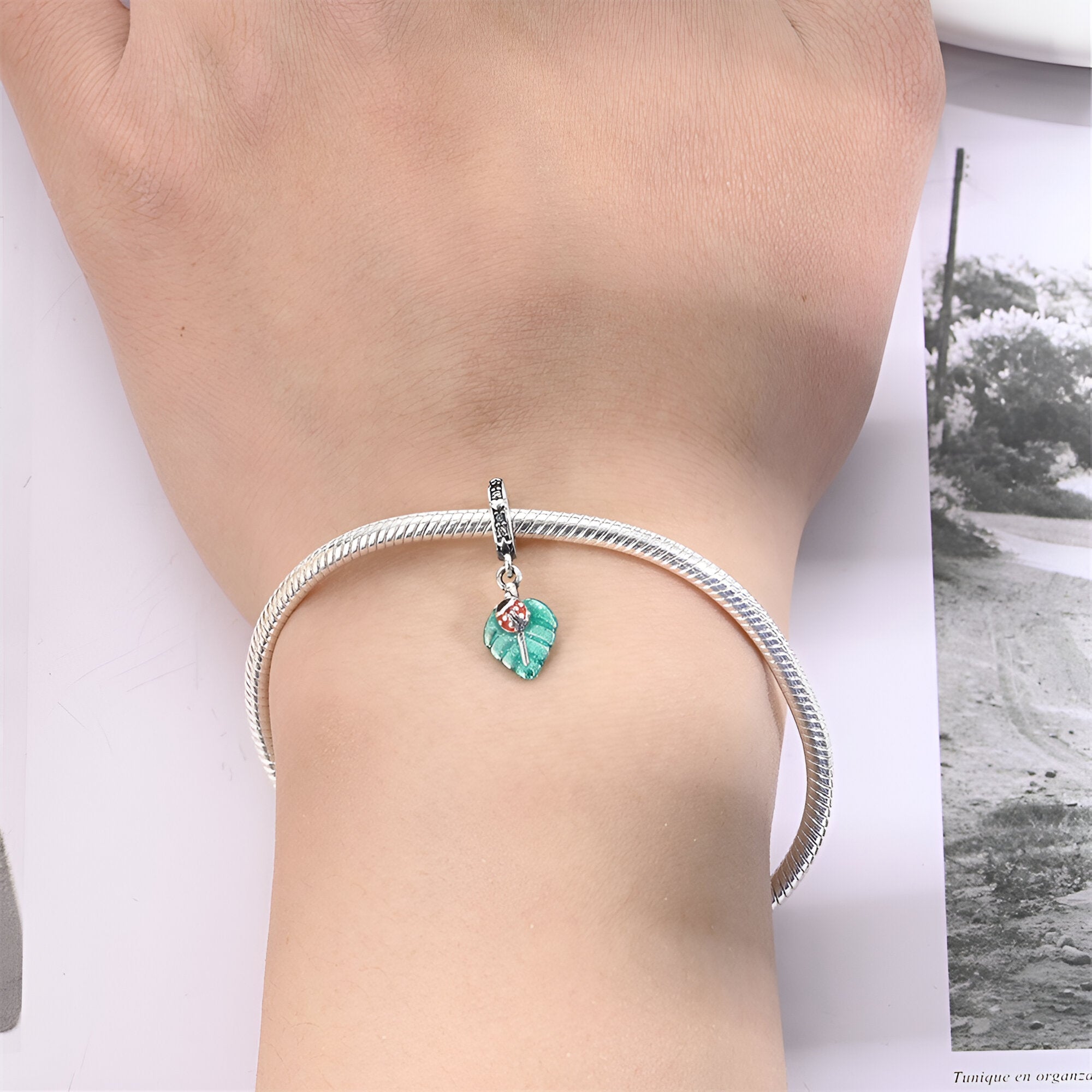Charm pendentif argenté avec coccinelle rouge sur feuille verte porté sur bracelet snake argenté.