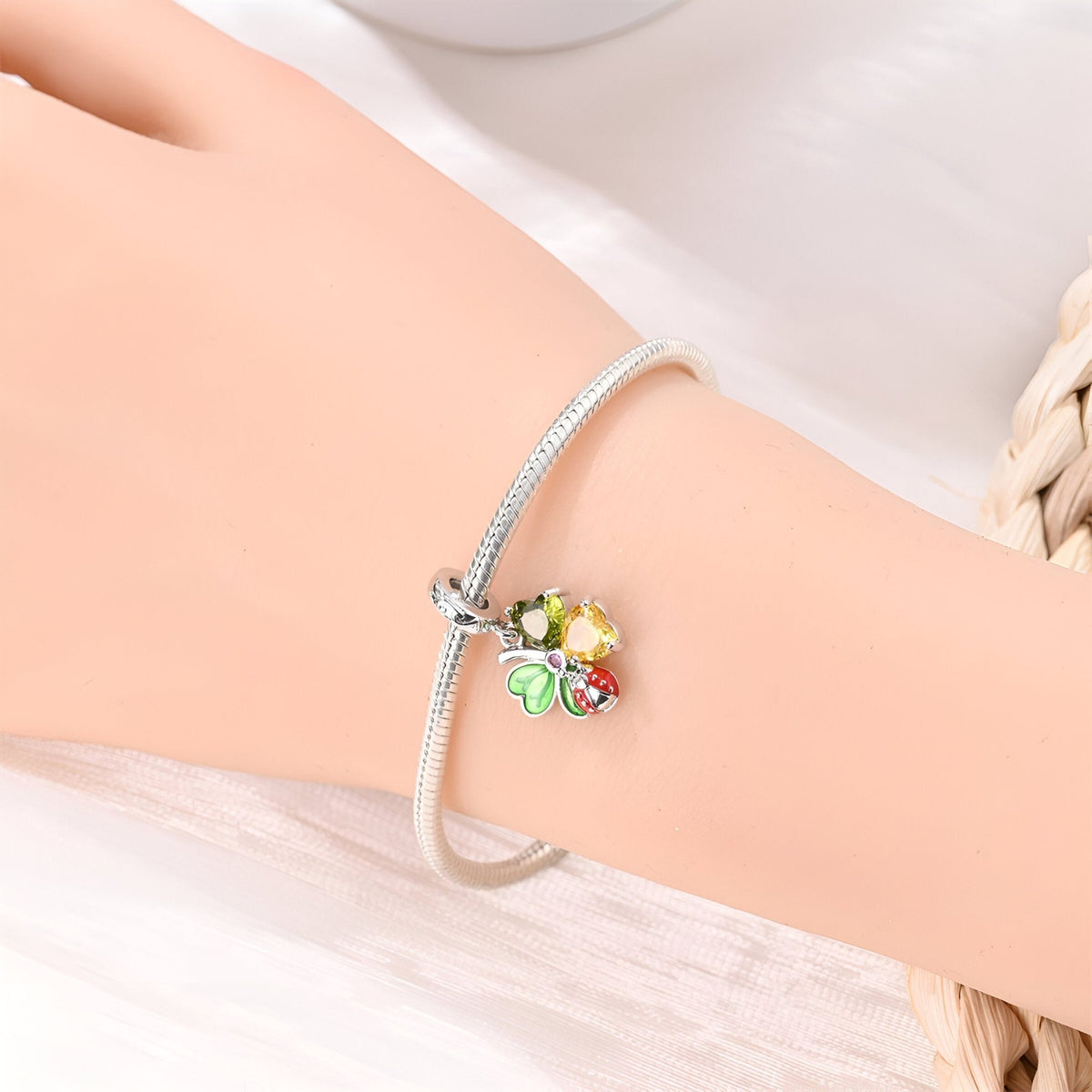 Bracelet argenté avec pendentif coccinelle rouge sur trèfle vert et jaune.