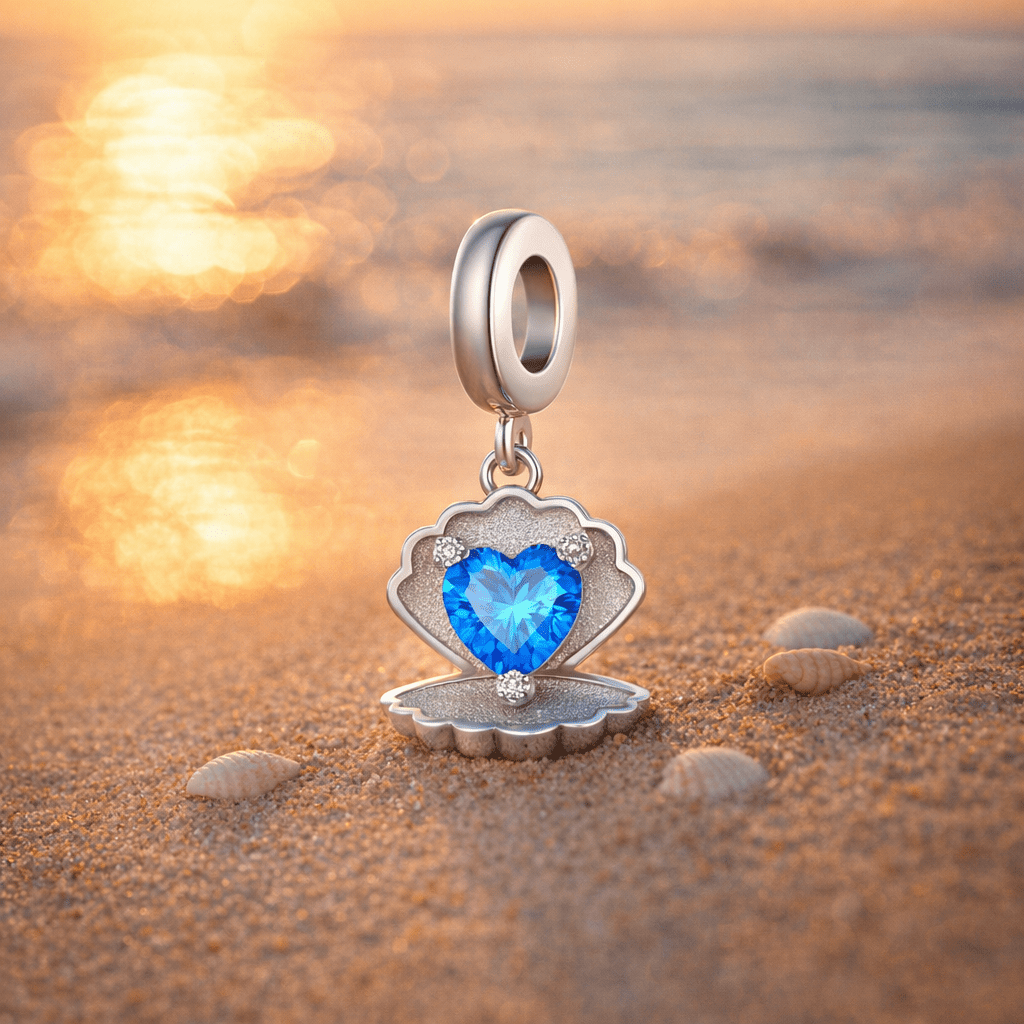 Charm Conchilia coquillage cœur bleu posé sur le sable doré au coucher du soleil avec petits coquillages
