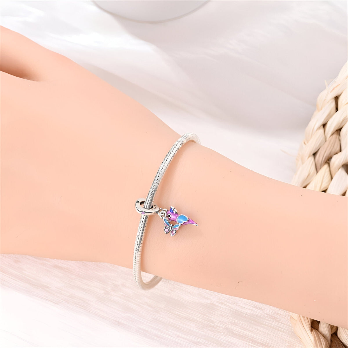 Bracelet argent fin avec pendentif oiseau et papillon coloré sur poignet féminin.