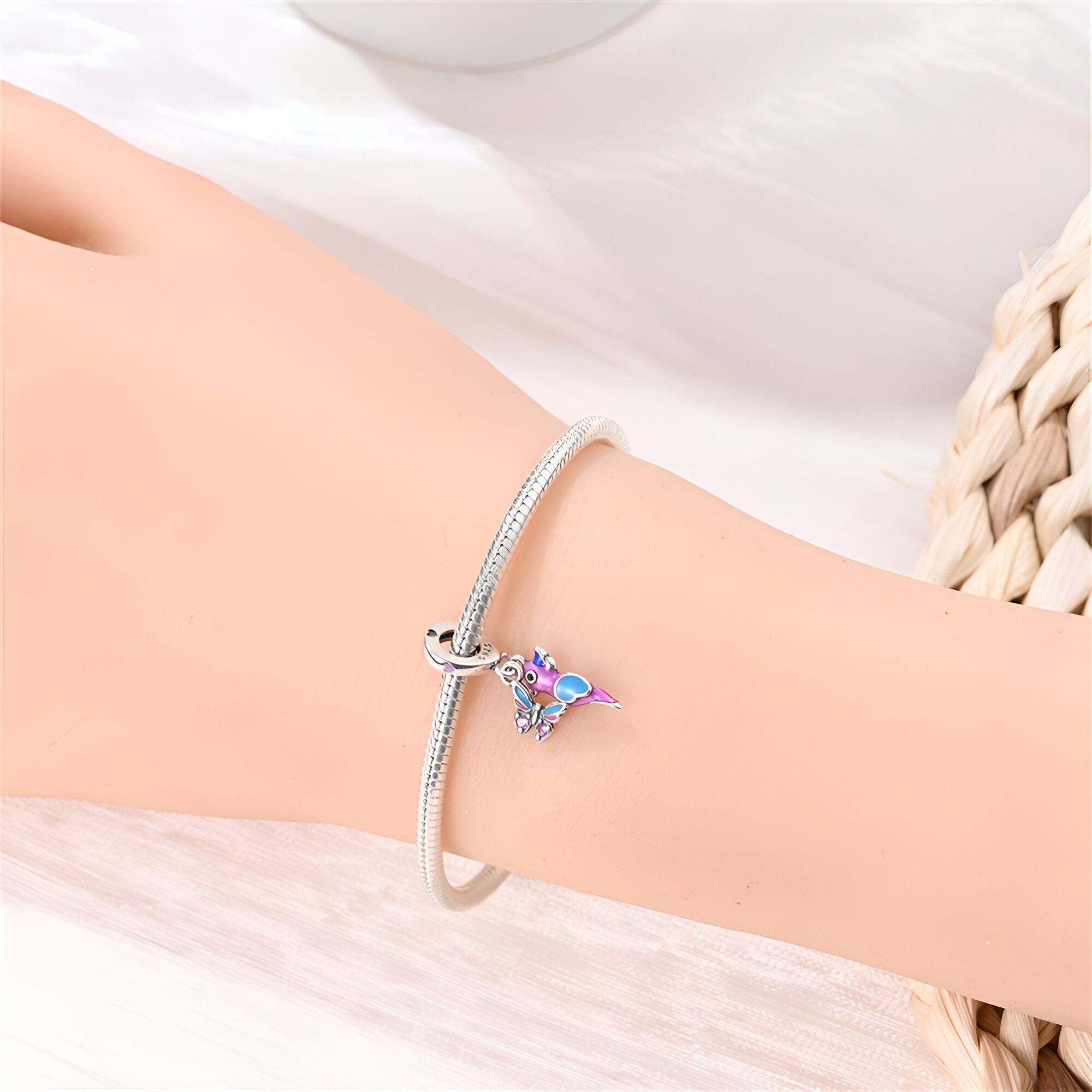 Bracelet argent fin avec pendentif oiseau et papillon coloré sur poignet féminin.