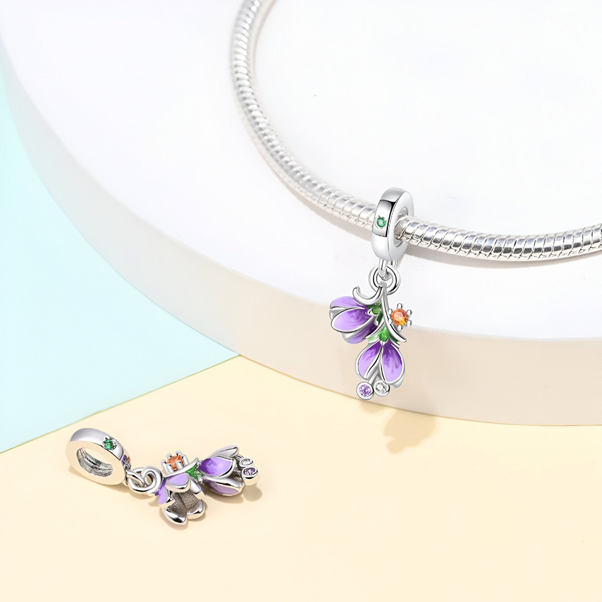 Charm pendentif argent avec fleurs de violette violettes émaillées et détail orange suspendu à un bracelet serpent.