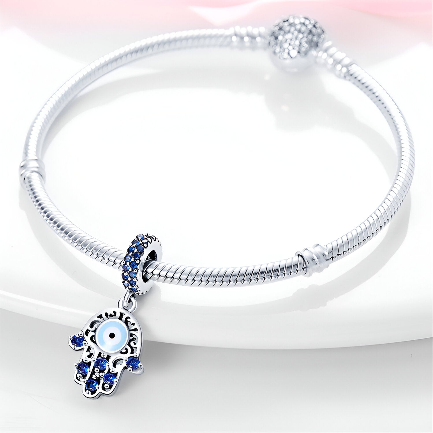 Bracelet argent avec pendentif main de Fatma ornée de pierres bleues et œil protecteur central.