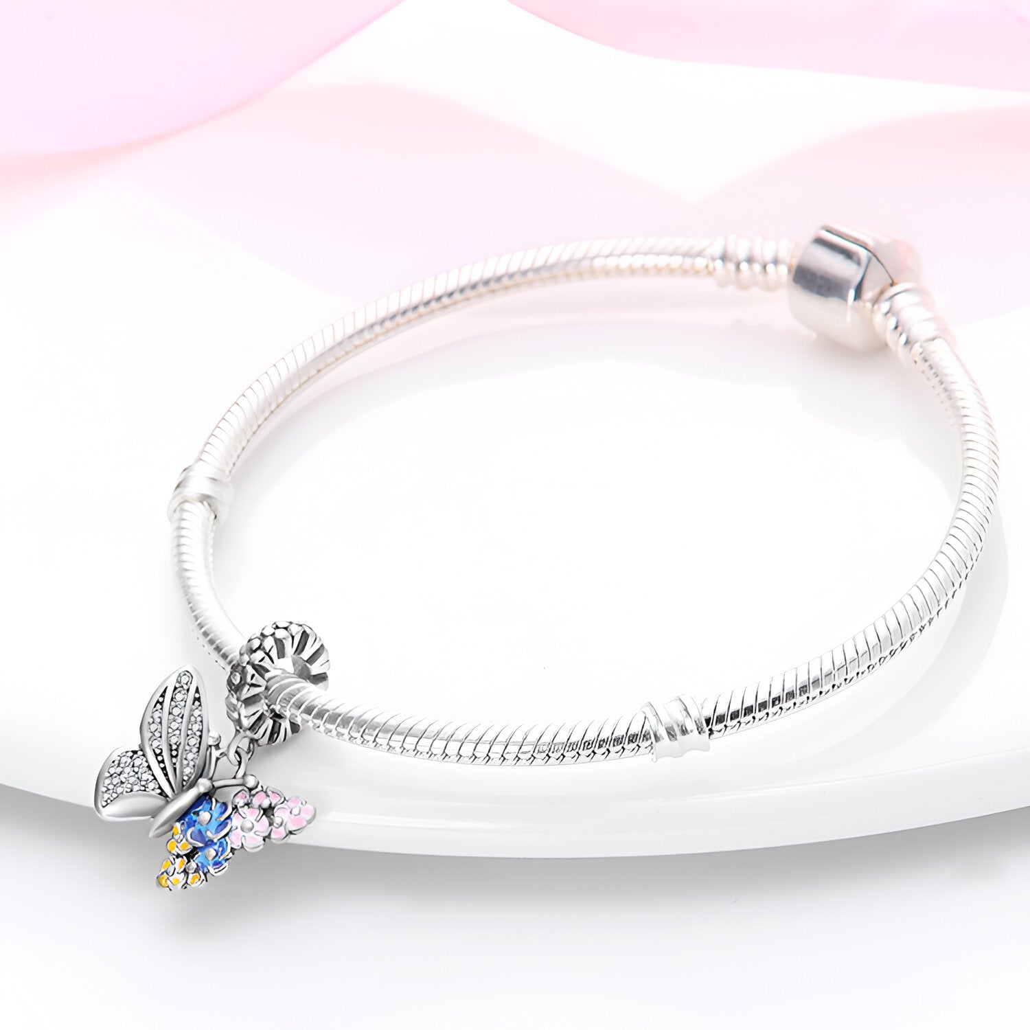 Bracelet argenté avec pendentif papillon aux ailes décorées de fleurs colorées bleu et rose.