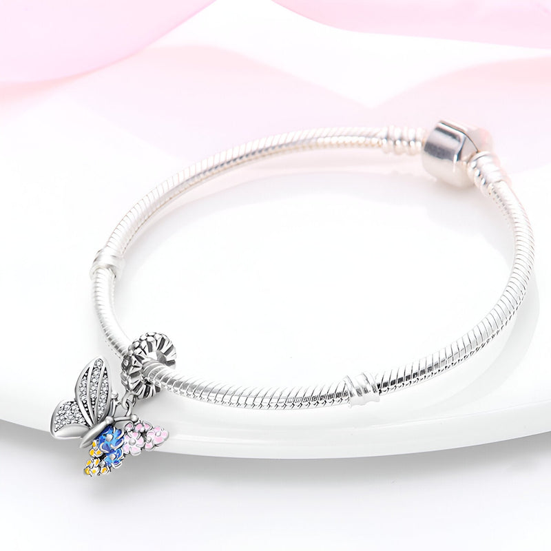 Bracelet argenté avec pendentif papillon aux ailes décorées de fleurs colorées bleu et rose.