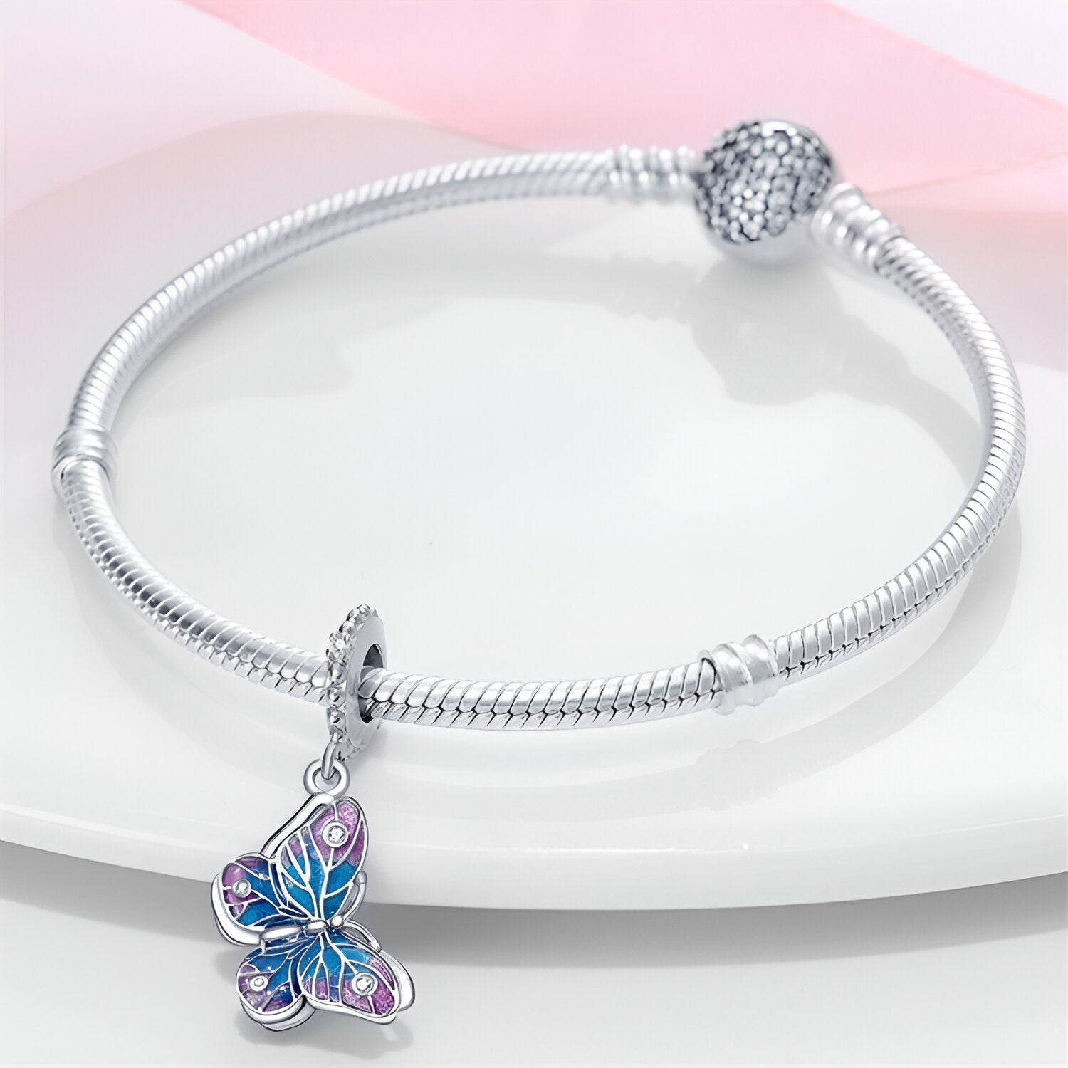 Bracelet en argent avec pendentif papillon bleu et rose aux détails gravés élégants.