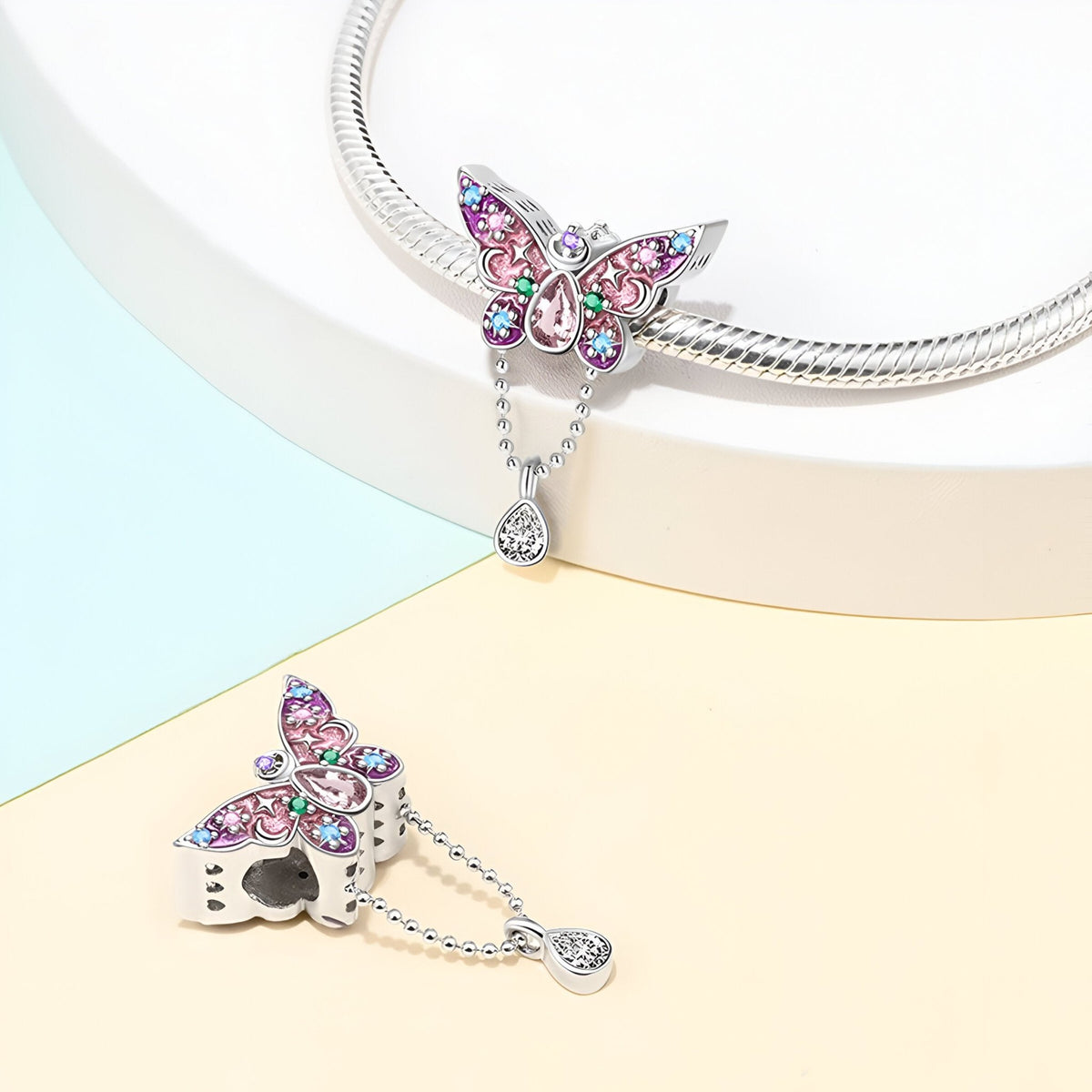 Pendentif papillon argenté orné de cristaux rose et bleu sur chaîne serpent brillante.
