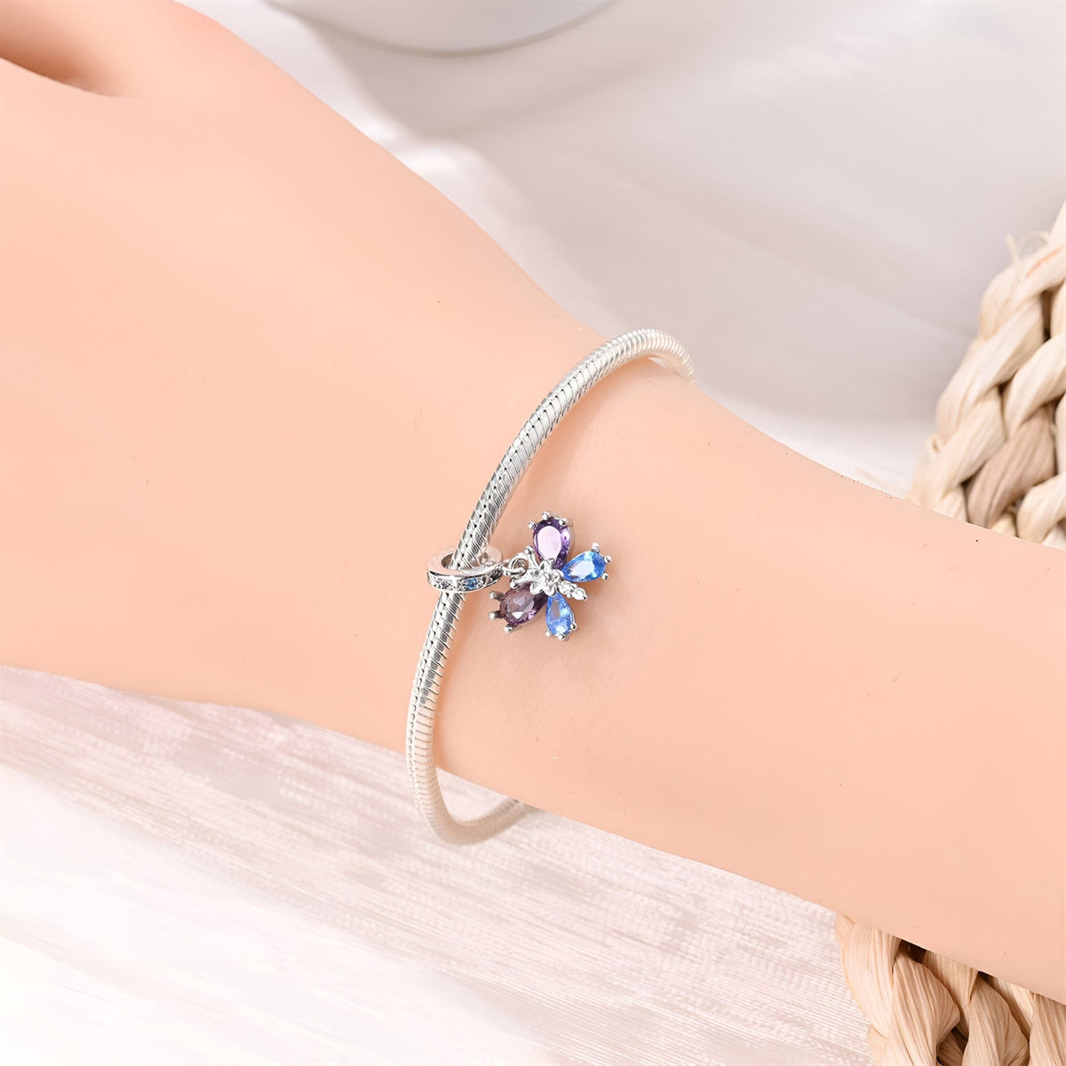 Charm pendentif papillon coloré en métal argenté avec pierres bleues, porté sur un bracelet fin en métal argenté.