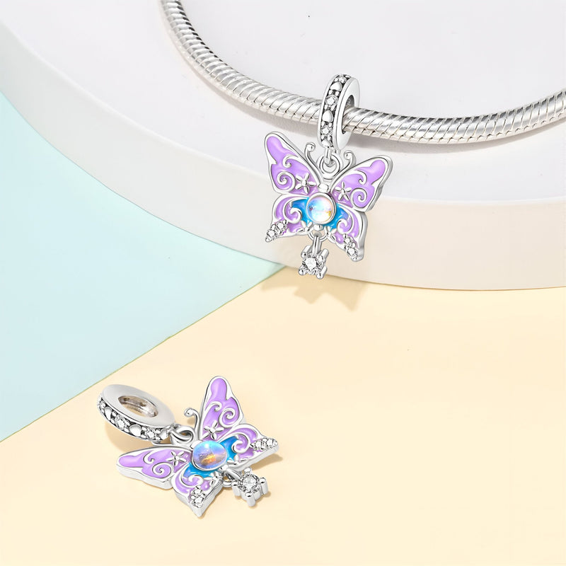 Charm pendentif papillon en métal argenté avec émail violet et strass bleu brillant.