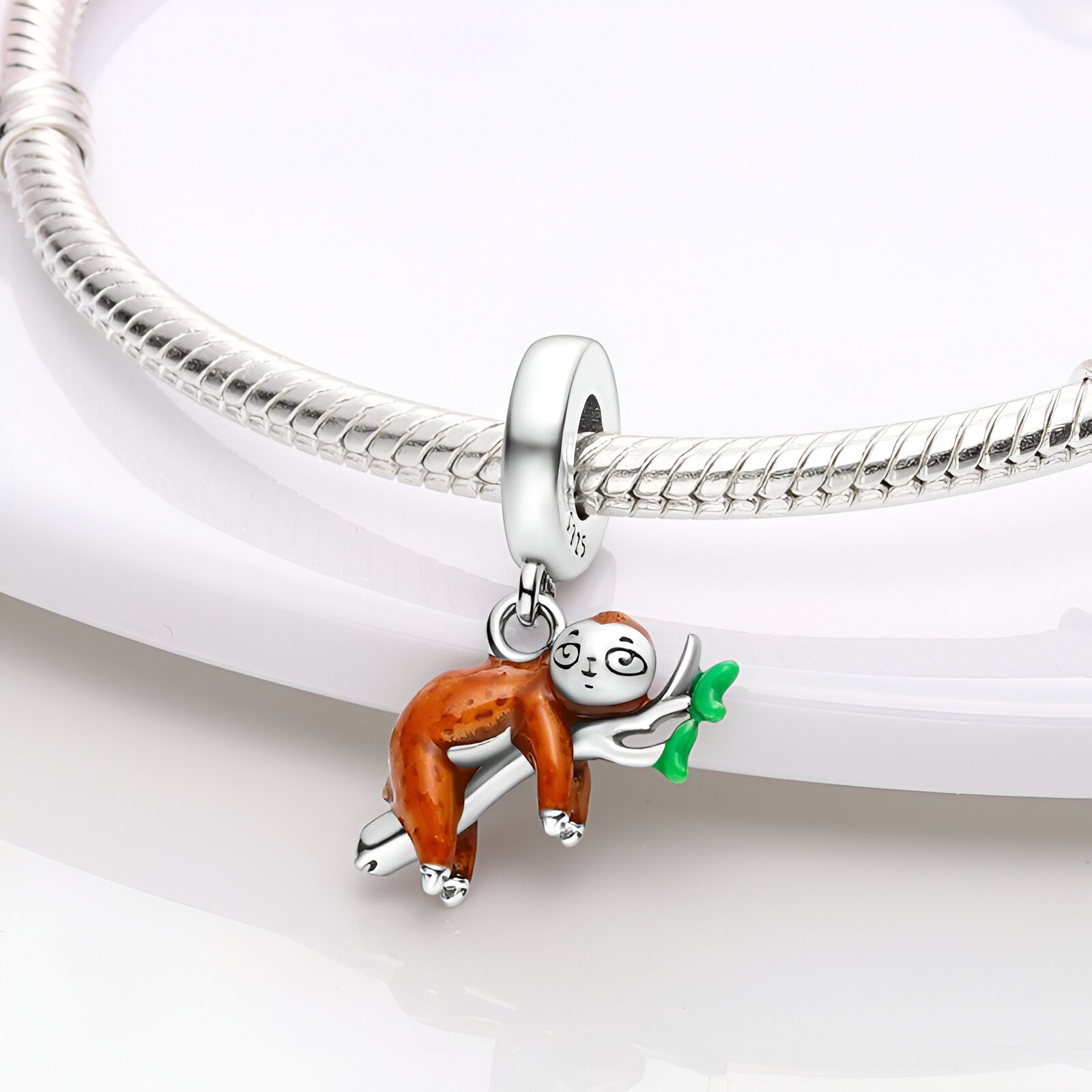 Charm pendentif paresseux émaillé marron et blanc tenant une feuille verte sur bracelet argenté.
