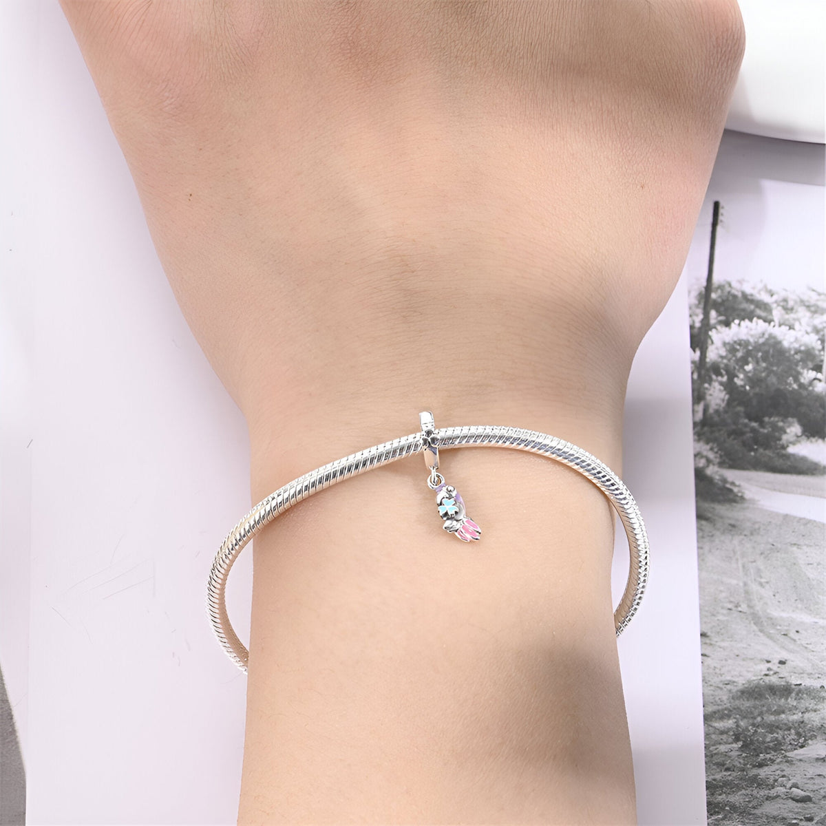Bracelet argenté avec charm perroquet coloré suspendu au poignet féminin.